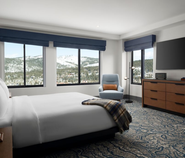 Hotel bedroom with a king bed, blue accents, and a mountainside view through large windows moldings.