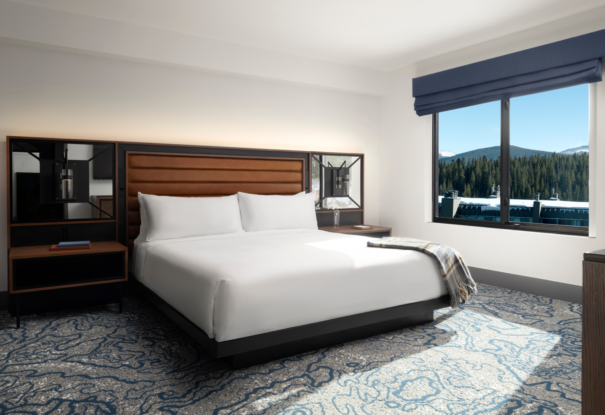 King bedroom with plush white bedding, wood headboard, and mountain view window at Hotel Alpenrock.