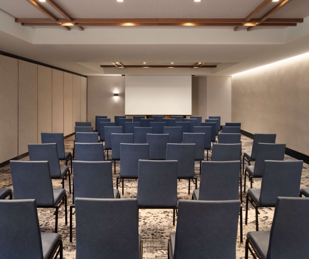 Theater-style meeting room at Hotel Alpenrock with rows of blue chairs facing a projection screen.
