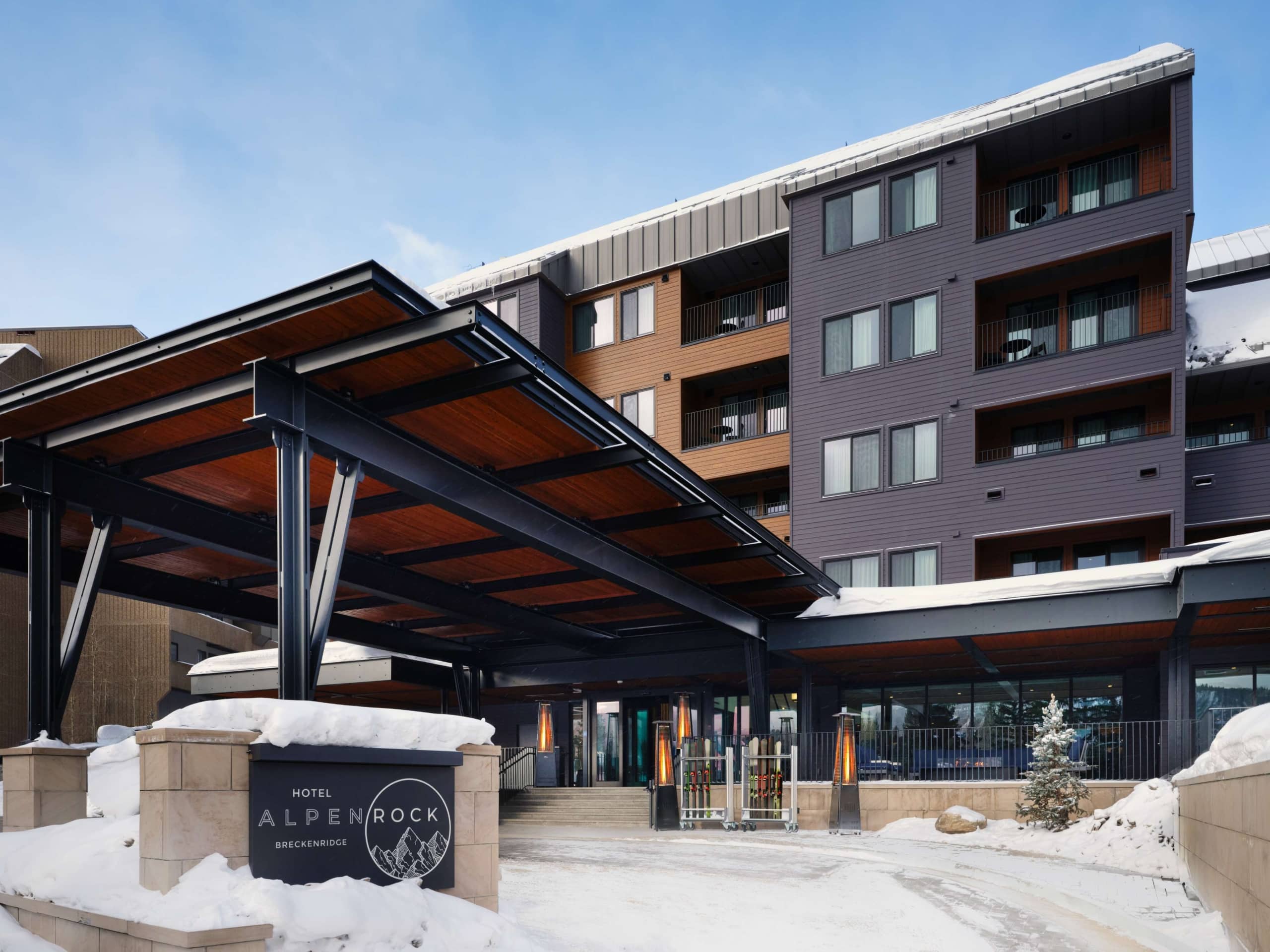 Daytime exterior of Hotel Alpenrock in Breckenridge with covered entrance, modern mountain architecture, and fresh snow.