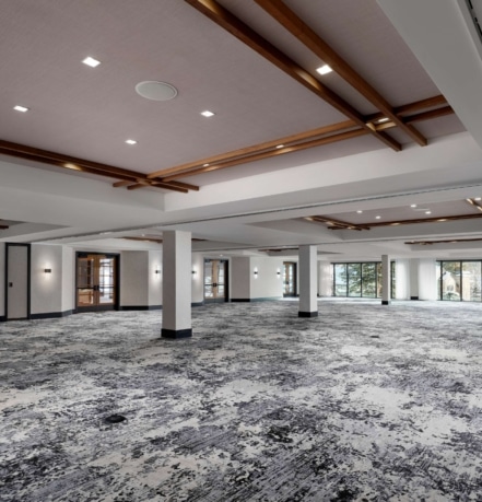 Expansive empty ballroom at Hotel Alpenrock with high beamed ceilings, large windows, and patterned carpet.