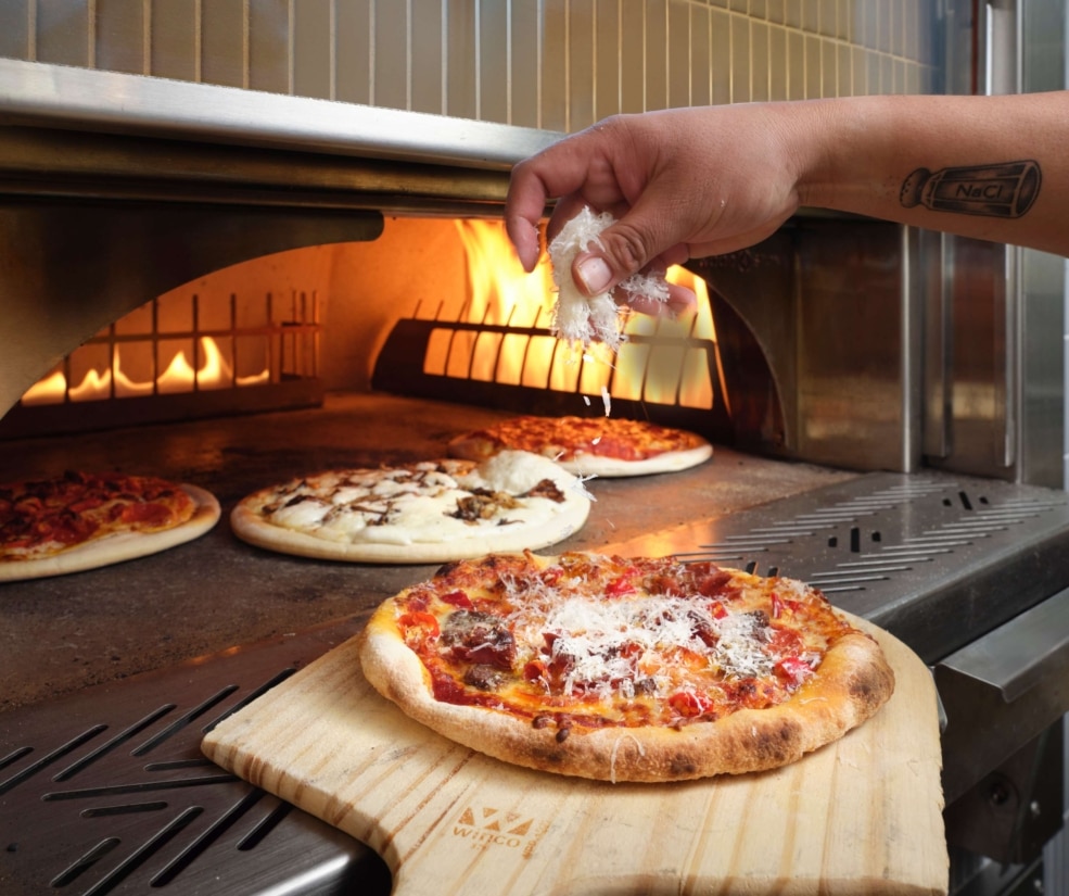 Wood-fired pizza being finished with grated cheese in the oven at The Edwin inside Hotel Alpenrock.