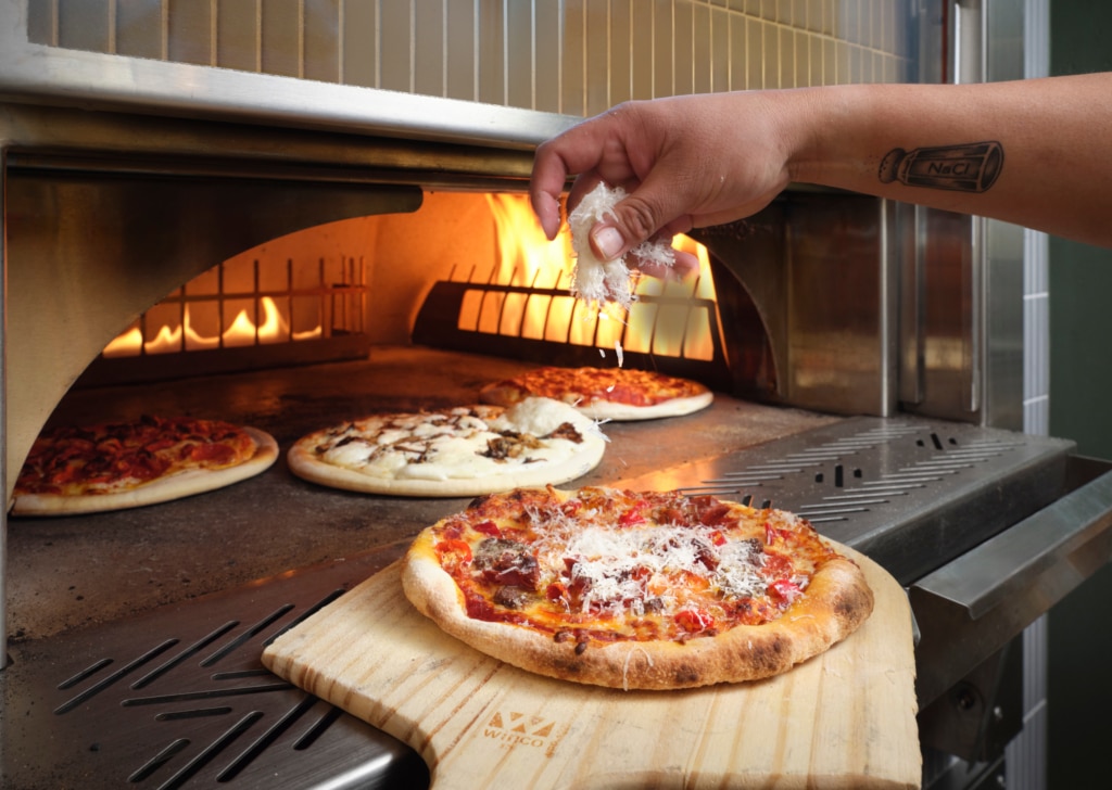Wood-fired pizza being finished with grated cheese in the oven at The Edwin inside Hotel Alpenrock.