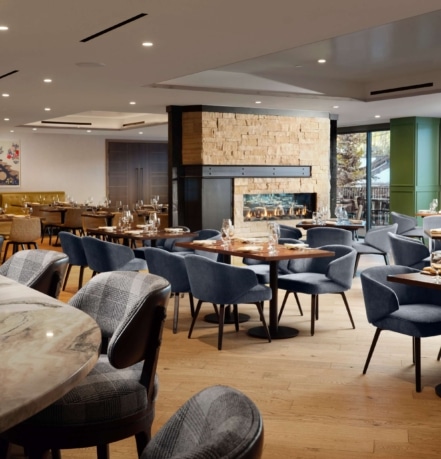 Elegant dining room at The Edwin inside Hotel Alpenrock, featuring a stone fireplace, set tables, and modern seating with large windows.