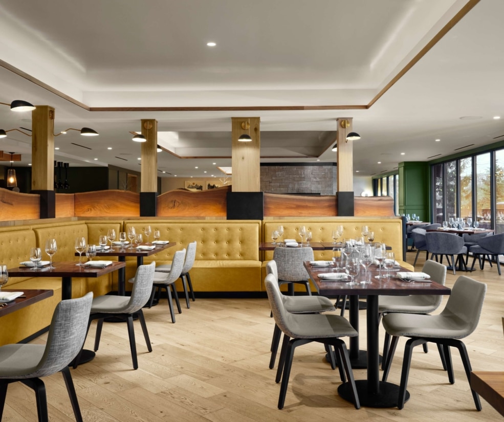 Dining room at The Edwin inside Hotel Alpenrock, featuring mustard-yellow banquettes, wood accents, and neatly set tables with wine glasses.