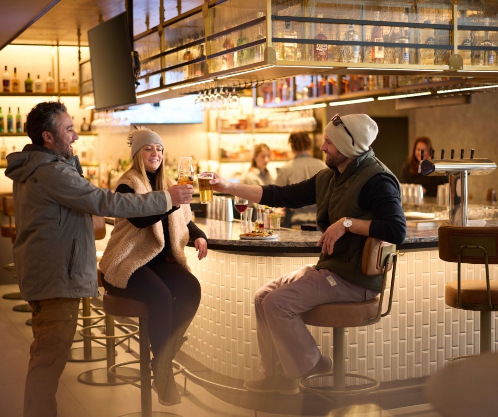 Guests enjoying drinks and conversation at The Edwin inside Hotel Alpenrock, gathered around the bar in a warm, inviting atmosphere.