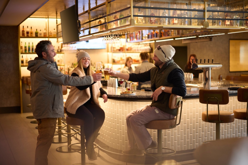 Guests enjoying drinks and conversation at The Edwin inside Hotel Alpenrock, gathered around the bar in a warm, inviting atmosphere.