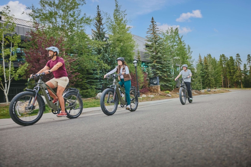 Guests riding electric bikes along the road at Hotel Alpenrock, surrounded by trees and mountain scenery.