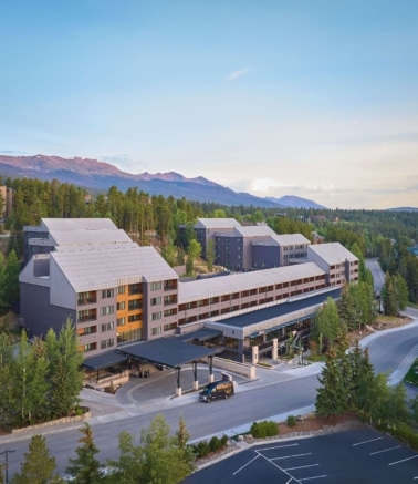 Aerial view of Hotel Alpenrock with its main entrance, surrounding pine forest, and mountain backdrop at sunset.