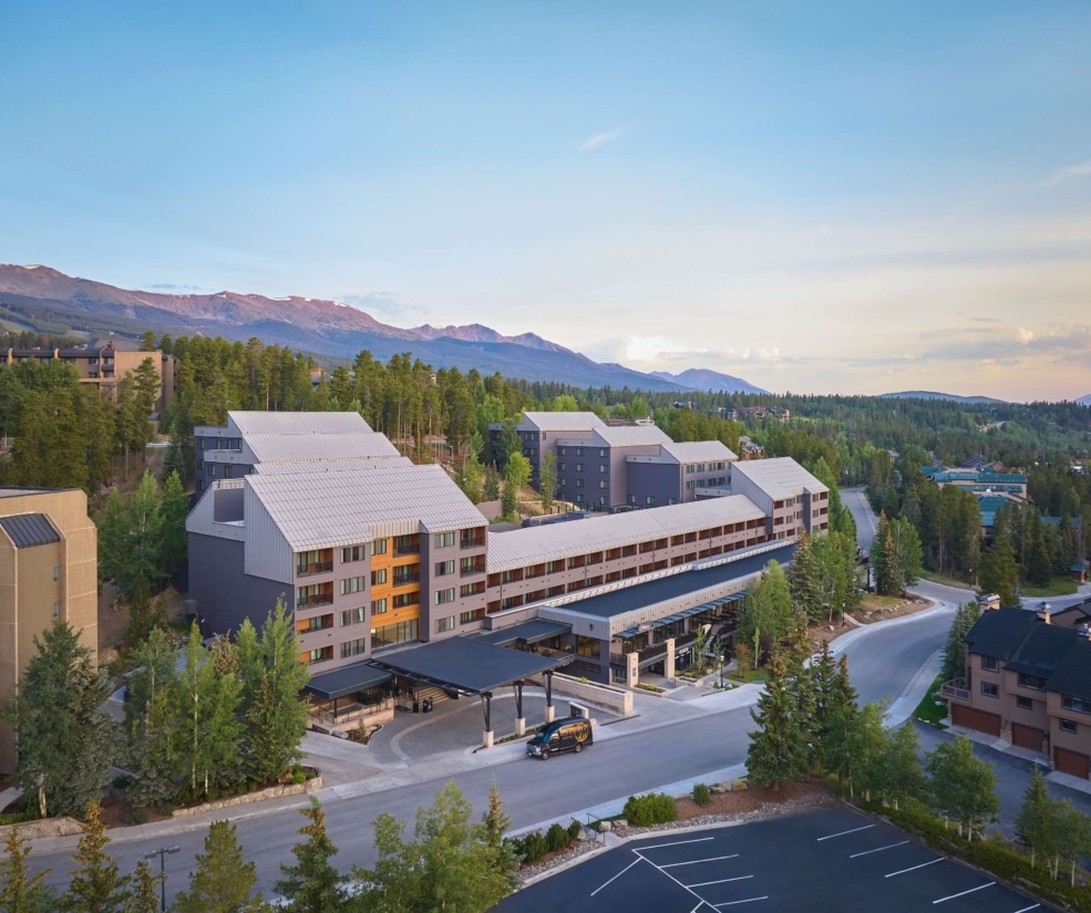 Aerial view of Hotel Alpenrock with its main entrance, surrounding pine forest, and mountain backdrop at sunset.
