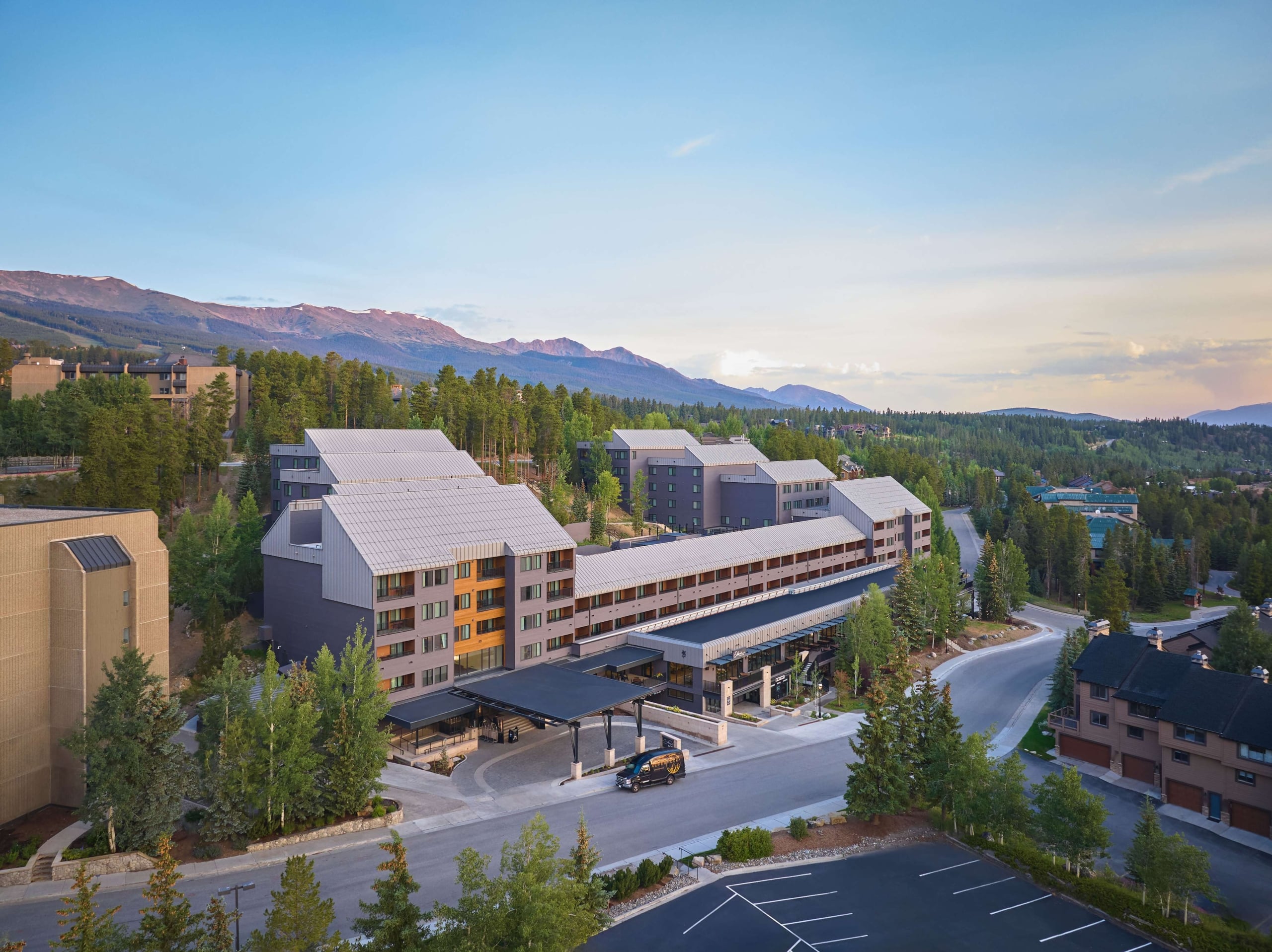 Aerial view of Hotel Alpenrock with its main entrance, surrounding pine forest, and mountain backdrop at sunset.