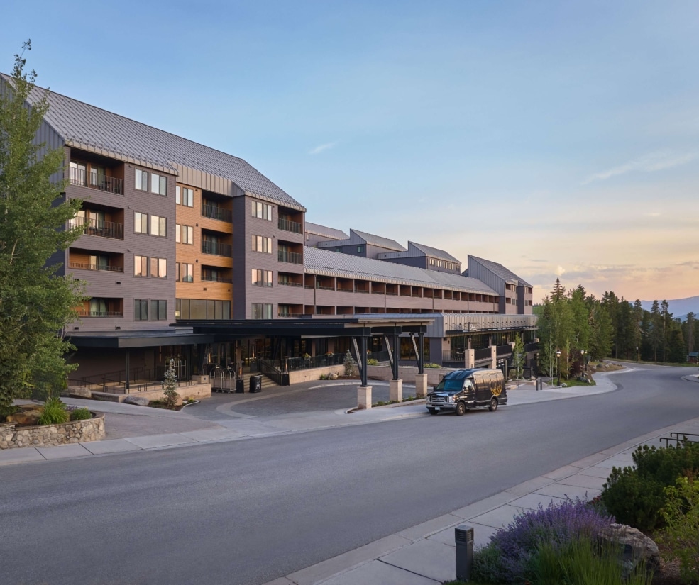 Exterior view of Hotel Alpenrock at dusk, featuring the main entrance, modern mountain architecture, and surrounding pine trees.