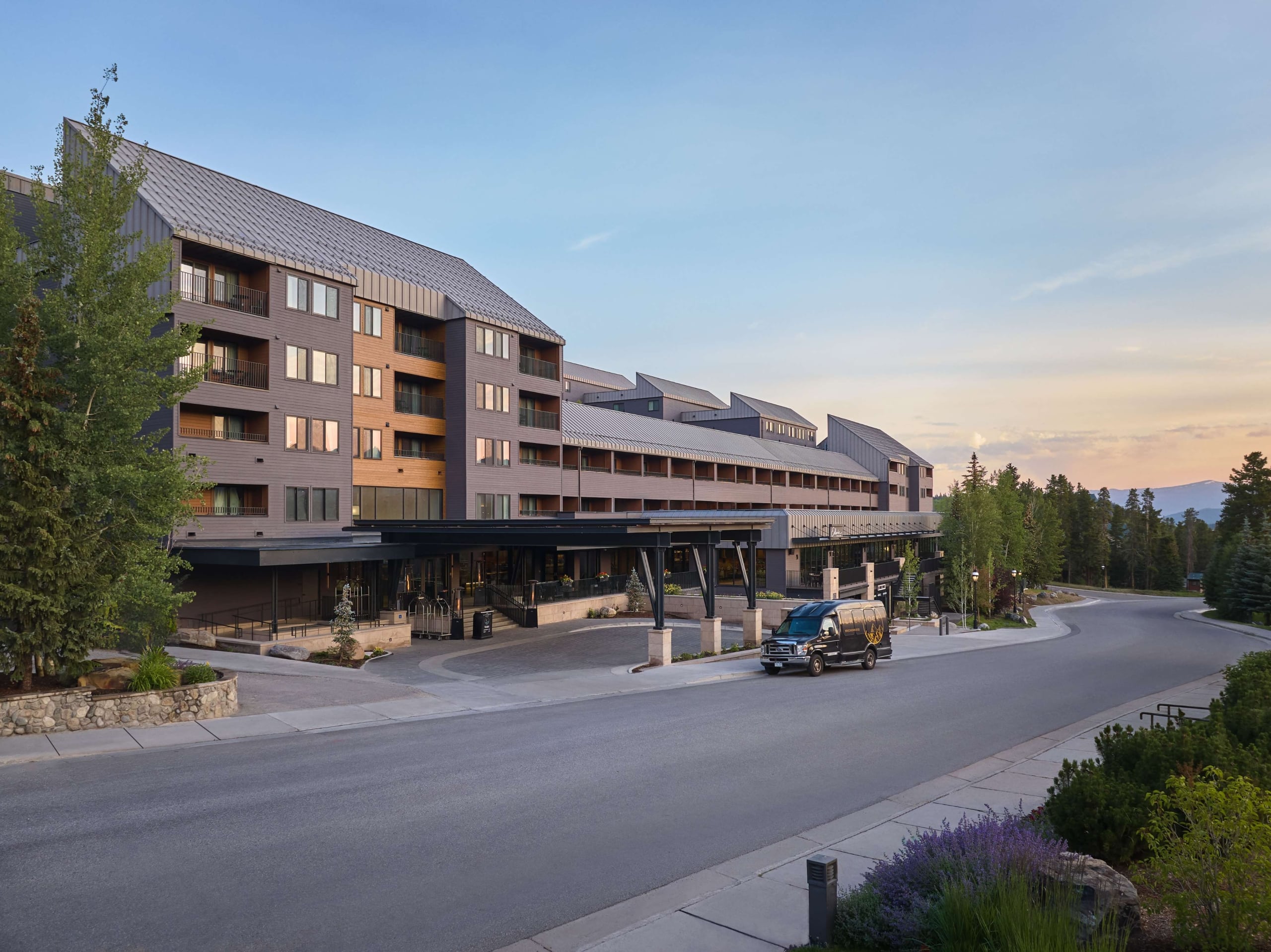 Exterior view of Hotel Alpenrock at dusk, featuring the main entrance, modern mountain architecture, and surrounding pine trees.