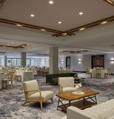 Spacious ballroom at Hotel Alpenrock with elegant high ceilings, wooden beams, round banquet tables, lounge seating, and large windows overlooking mountain views.