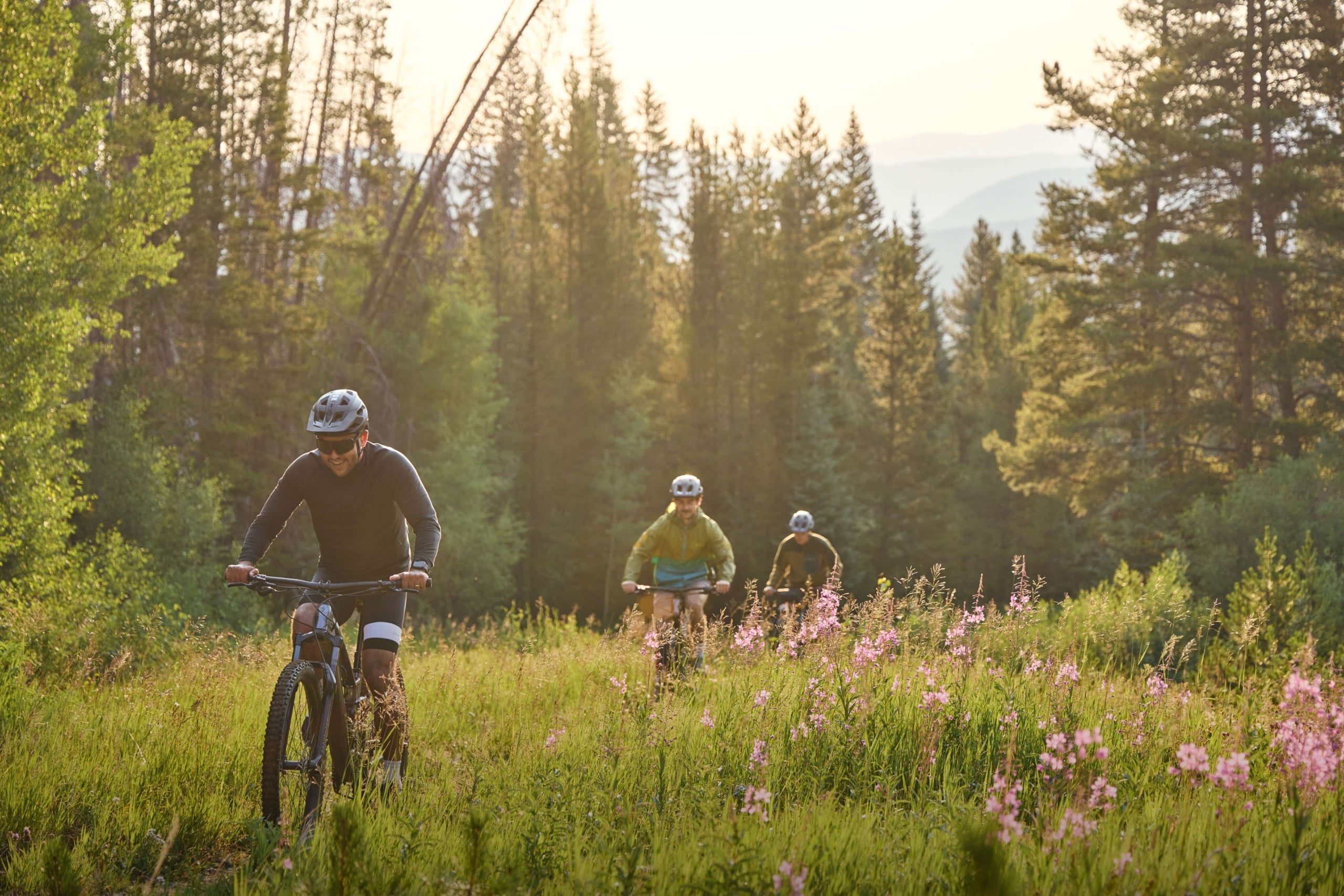 Guests mountain biking through a forest meadow near Hotel Alpenrock, surrounded by wildflowers and trees.