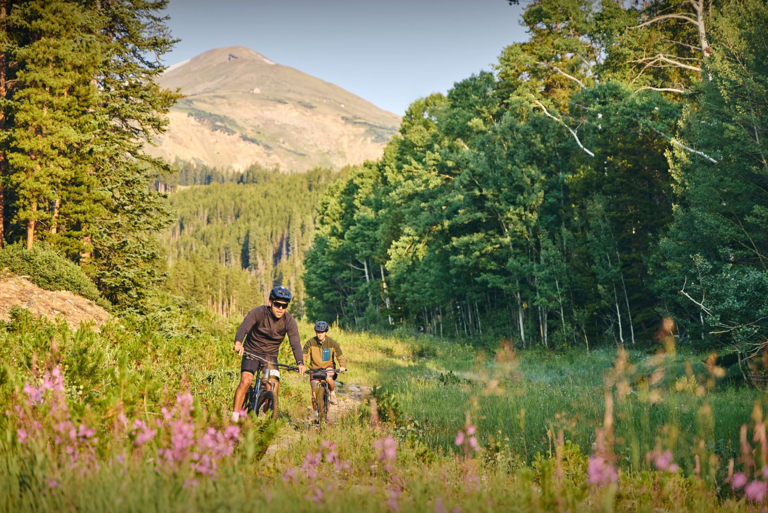 Guests mountain biking through a forest meadow near Hotel Alpenrock, surrounded by wildflowers and trees.