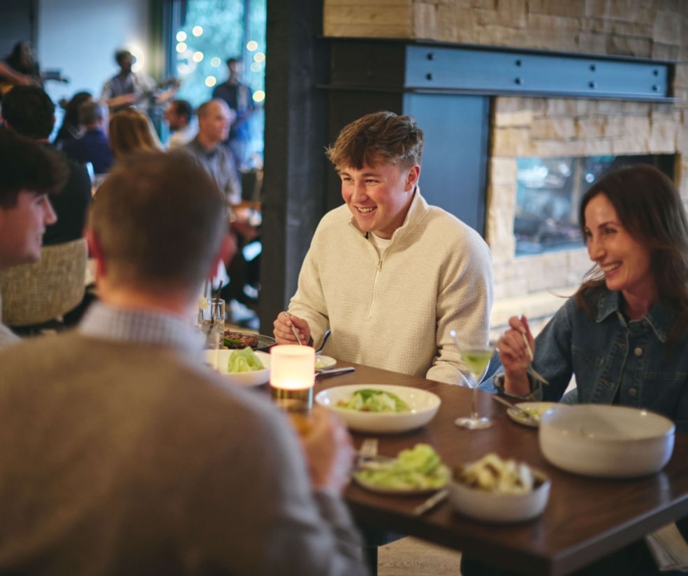 Guests laughing and enjoying dinner at Hotel Alpenrock, seated around a warmly lit table inside the restaurant.