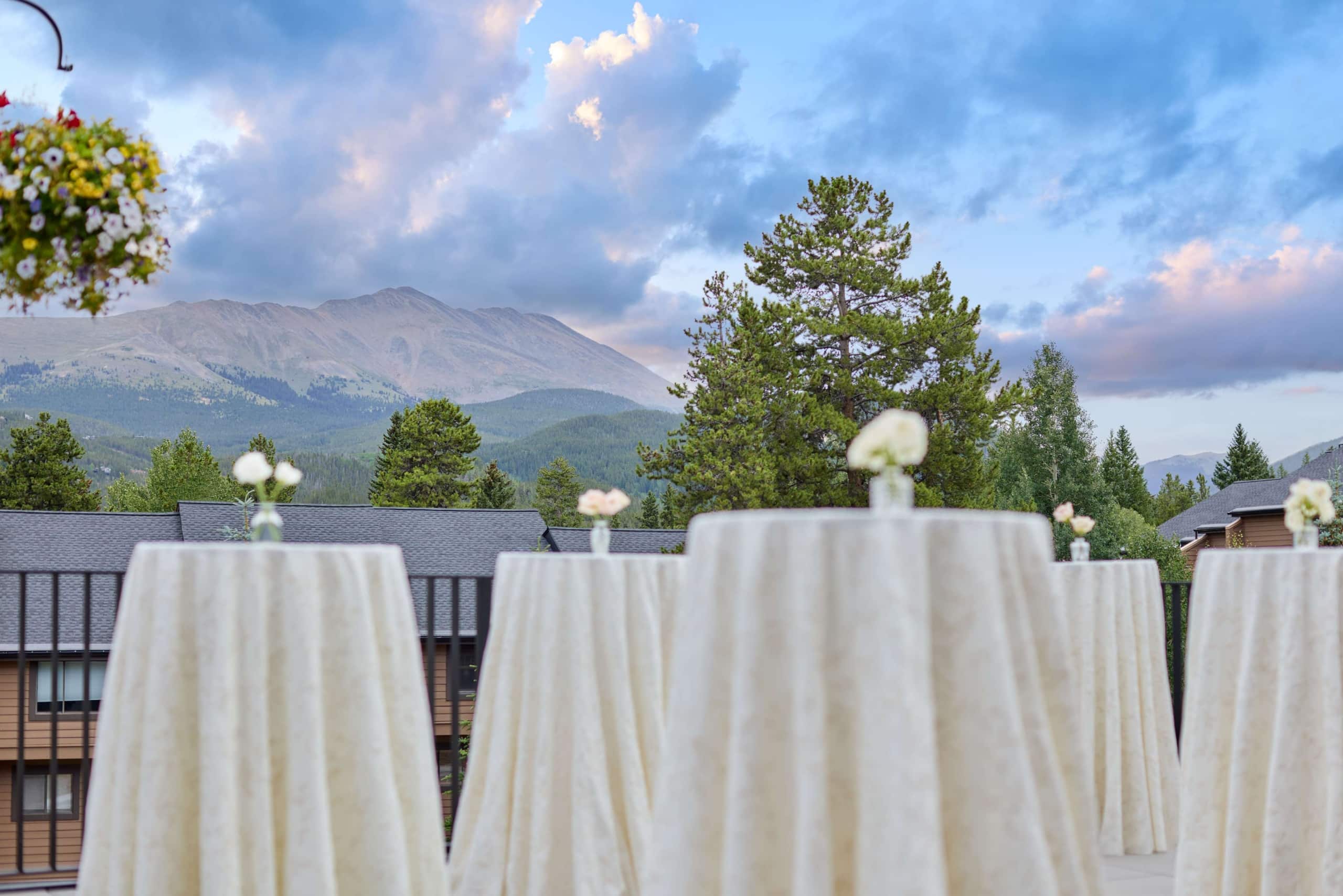 Outdoor event setup at Hotel Alpenrock with high-top cocktail tables, white linens, floral centerpieces, and dramatic sunset mountain views.