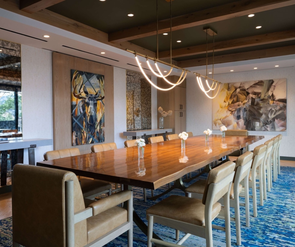 Sophisticated boardroom at Hotel Alpenrock with long live-edge wooden table, leather chairs, large abstract art, and exposed beam ceiling.