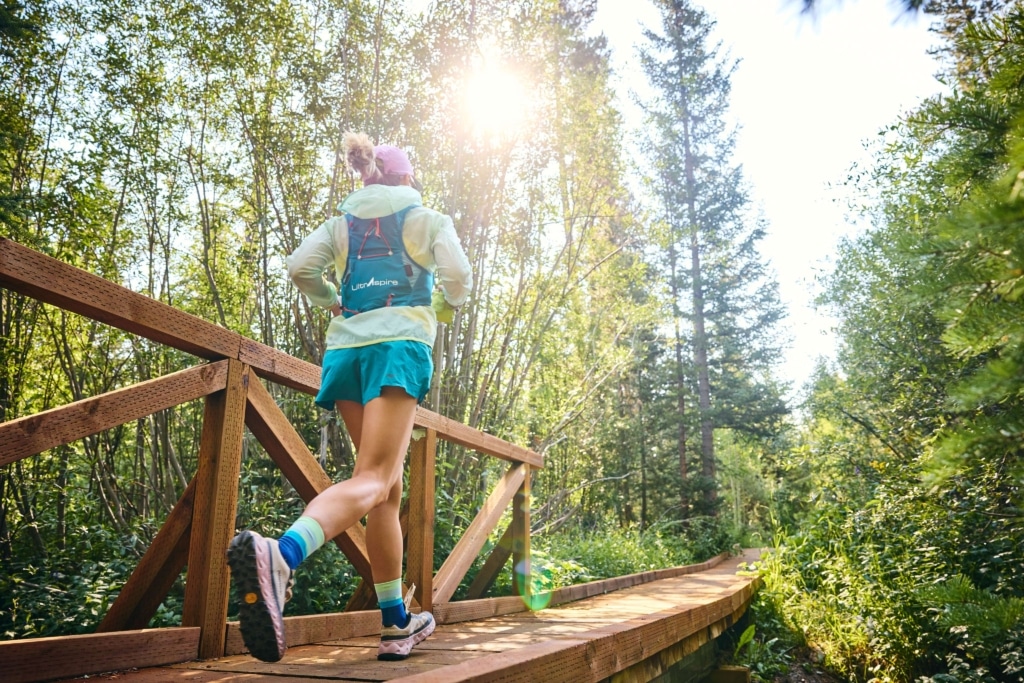 Trail runner crossing a wooden bridge on a forest path near Hotel Alpenrock in summer sunlight.