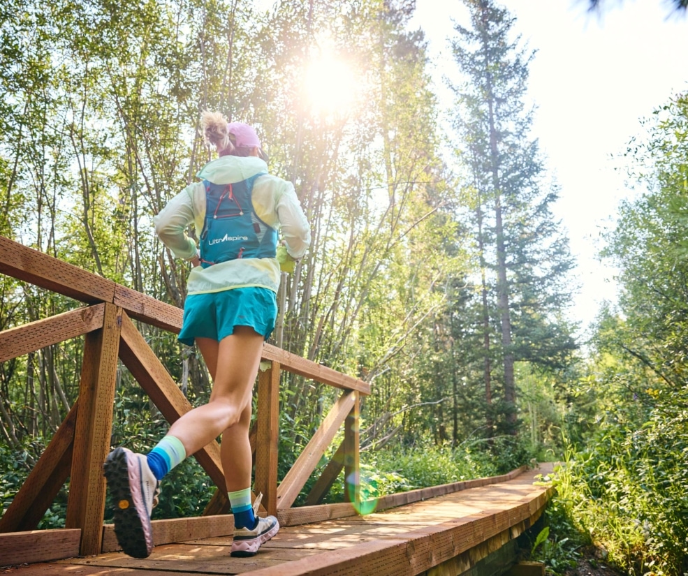Trail runner crossing a wooden bridge on a forest path near Hotel Alpenrock in summer sunlight.