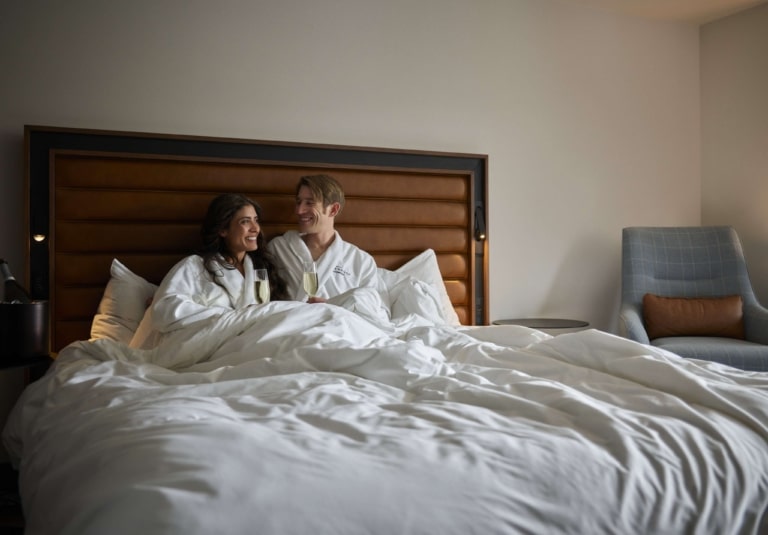 Couple enjoying champagne in bed inside a Hotel Alpenrock guest room.