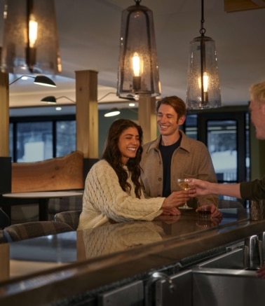 Guests enjoying drinks at the Hotel Alpenrock bar, sharing a relaxed moment under warm pendant lighting in a cozy, modern mountain setting.