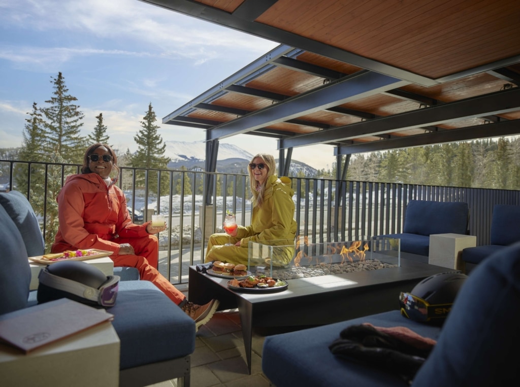 Guests enjoying après-ski drinks by the outdoor fire pit on the Hotel Alpenrock patio with mountain views.