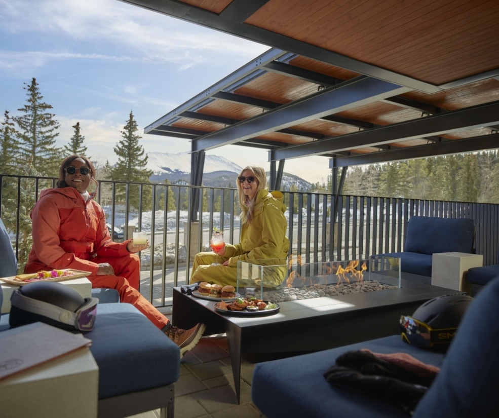 Guests enjoying après-ski drinks by the outdoor fire pit on the Hotel Alpenrock patio with mountain views.