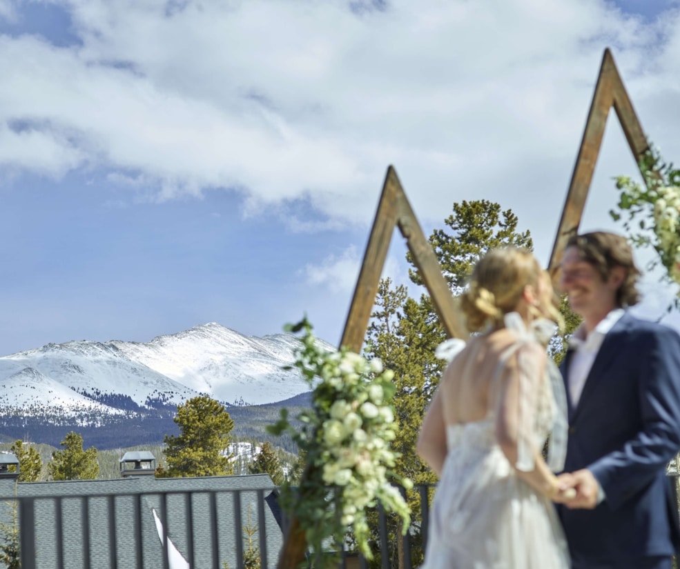 Romantic outdoor wedding ceremony at Hotel Alpenrock with a wooden triangular arch, floral accents, and breathtaking snowy mountain views.