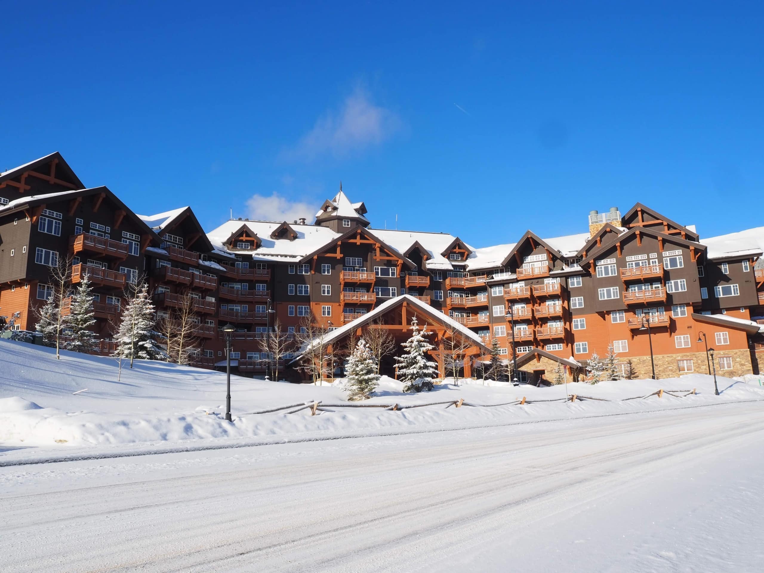 Snow-covered alpine hotel complex with wooden balconies under a clear blue sky.