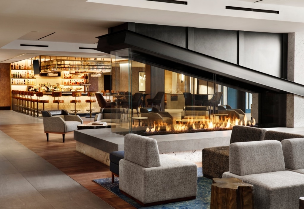Modern lounge with a bar on the left, glass partition, and a long gas fireplace running through the seating area
