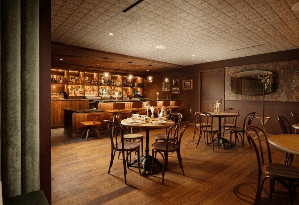 Warm, wood-floored bar and dining area with round tables and bentwood chairs, dim lighting at a cozy restaurant barh.