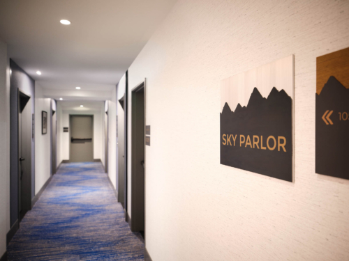 Hotel hallway with blue patterned carpet and framed art along the right wall at waist height